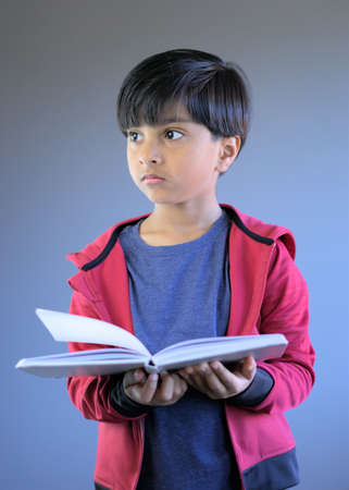 Portrait of child holding book looking away from lens. Serious expression smart kid with book.の写真素材
