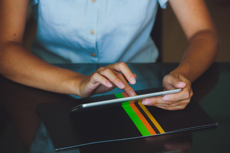 One light-skinned hand belonging to a woman holds a large tablet while the other hand uses a pointer finger to access something on the tablets touch screen display. The tablet has a gray case and a glass screen. The woman in blue shirt.の写真素材