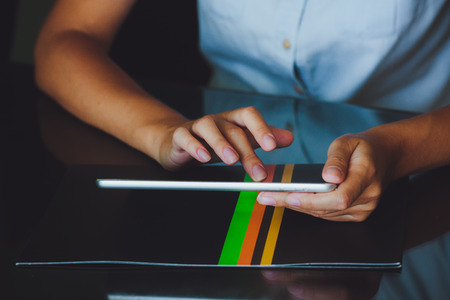 One light-skinned hand belonging to a woman holds a large tablet while the other hand uses a pointer finger to access something on the tablets touch screen display. The tablet has a gray case and a glass screen. The woman in blue shirt.の写真素材