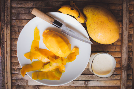 freshness fruit mango  lying on a white plate with knife. Fresh shake with milk and straw on brown board rusticの写真素材