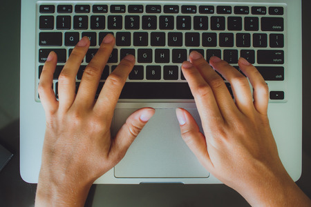 A woman's hands are typing on a laptop computer keyboard. The monitor is visible in the image, but it is not clear what she is working on.の写真素材