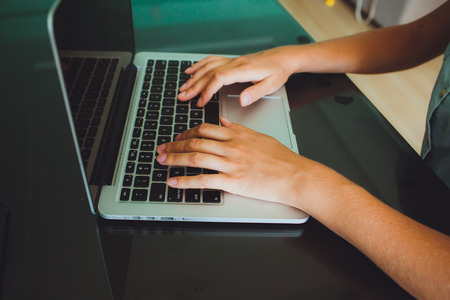A woman's hands are typing on a laptop computer keyboard. The monitor is visible in the image, but it is not clear what she is working on.の写真素材