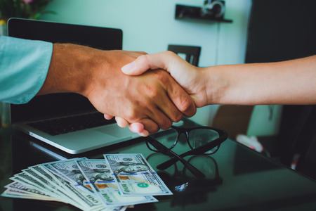 People at work: man and woman hand shaking at a meeting. Closeup shot of a two businesspeople shaking hands, glasses , money, laptop on background.の写真素材