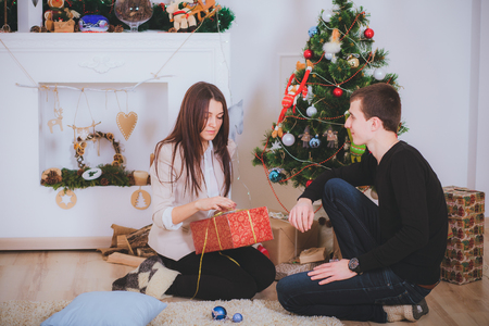 man gives a beautiful girl a Christmas present near Christmas treeの写真素材