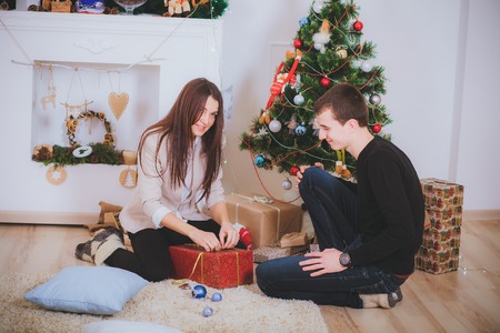 man gives a beautiful girl a Christmas present near Christmas treeの写真素材