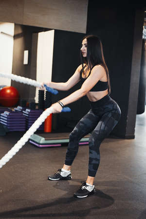 Young attractive brunette girl holding rope for crossfit. Female successfully practices workout and...