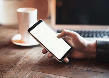 Young man with tattoo holding mobile, drinking coffee and working on PC