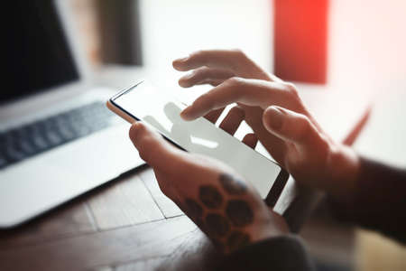 Young man with tattoo holding mobile phone and working on laptopの写真素材