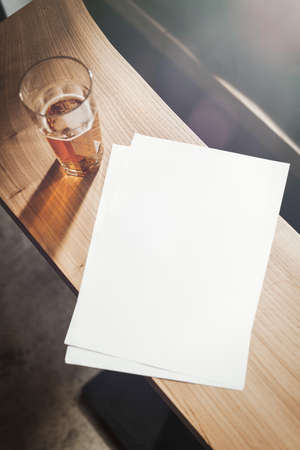 Glass of beer and blank sheet A4 are on wooden table.の写真素材