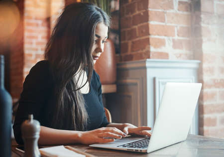Pensive young woman working on laptop in cafe.の写真素材