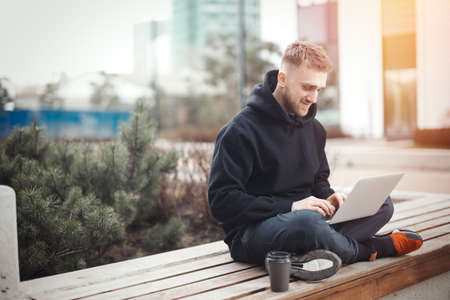 Smiling young man holding laptop on knees. Black coffee cup is next to him.