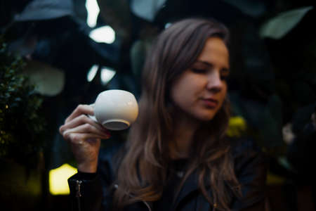 Young attractive girl drinking coffee. Coffee cup is on foreground and focus. girl is on background and blurred.の写真素材