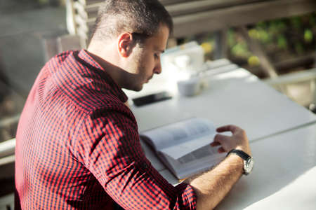 Young attractive man reading book at cafe.の写真素材