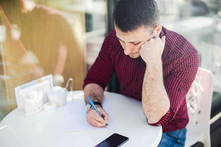 Young attractive man writing note at the paper at cafe.の写真素材