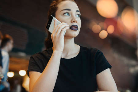 Young brunette girl with glasses talking by mobile phone in cafe at brunchの写真素材