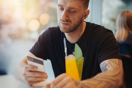 Attractive young man is reading message at g mobile phone and drinking lemonade.の写真素材