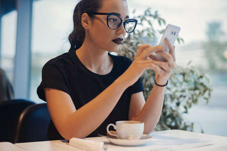Young attractive girl holding mobile phone and texting message at business lunch. Girl is on focus. mobile is blurred.の写真素材