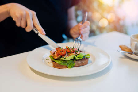 Young girl is eating bruschetta at business lunch. Food is on focus, cutlery is blurred.