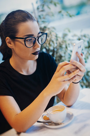 Young attractive girl holding mobile phone and typing sms at business lunch. Girl is on focus., phone is blurred.の写真素材