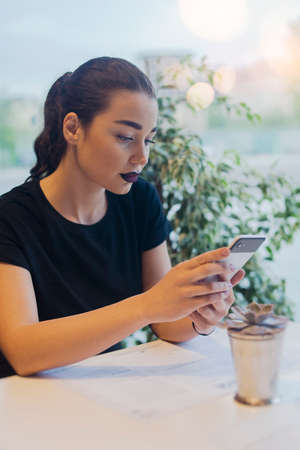 Young brunette girl holding mobile phone and texting message. Girl is on foreground and focus.の写真素材