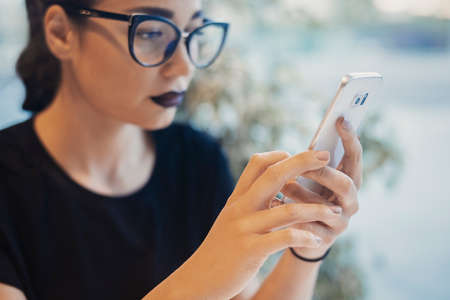 Young attractive girl holding mobile phone and texting message. Girl is blurred, mobile phone and hands are on focus.の写真素材