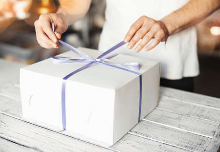 Young cook ties violet ribbon on white cake packagingの写真素材