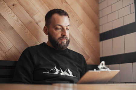 Young tattooed man holding menu at cafe.