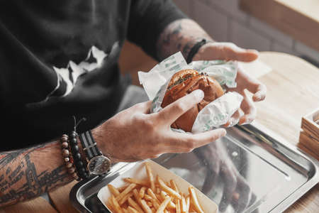 Young tattooed man eating burger at cafe.