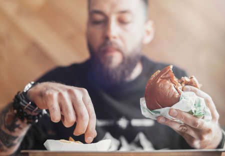 Young bearded man eating burger and french fries.