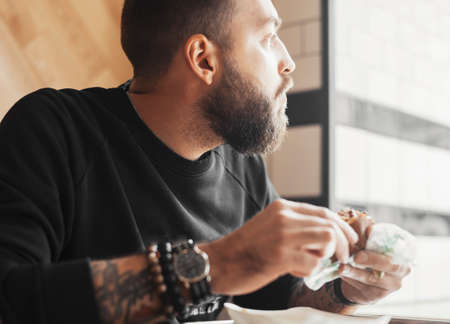Young bearded man eating burger close up.の写真素材