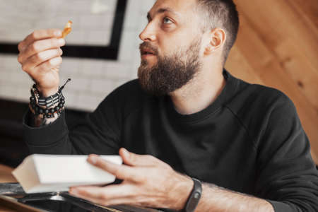 Young bearded man eating french fries close up.