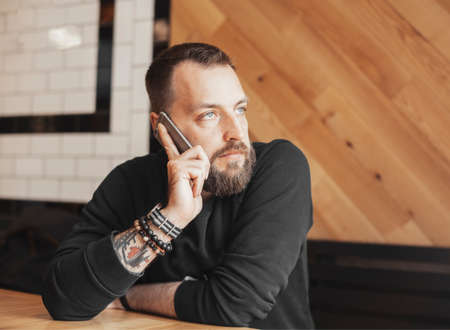 Bearded attractive tattooed man talking by phone in cafe close up.の写真素材