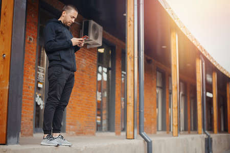 Bearded man standing next to red bricked building and staring at the screen.