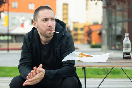 Bearded man with toothpick sits at the street.の写真素材