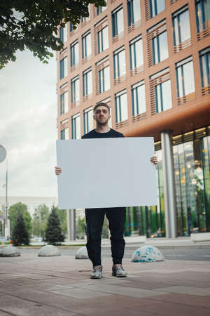 Young attractive man holding blank canvas and looking at the viewer. Front view.の写真素材