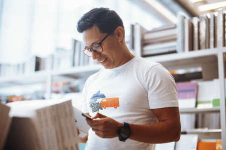 Young happy spectacled man reading book in bright modern book store.の写真素材