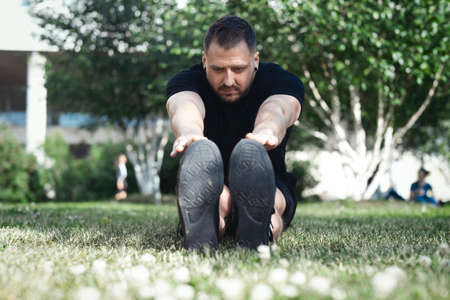 Attractive man in black sportwear doing stretching exercises outdoors in park.の写真素材
