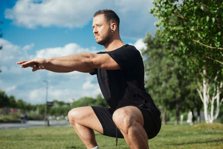 Young attractive man squatting outdoor in the park.の写真素材