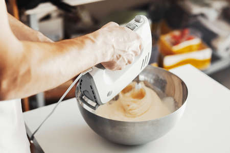 Whipped cream in metal bowl with mixer and hand.の写真素材