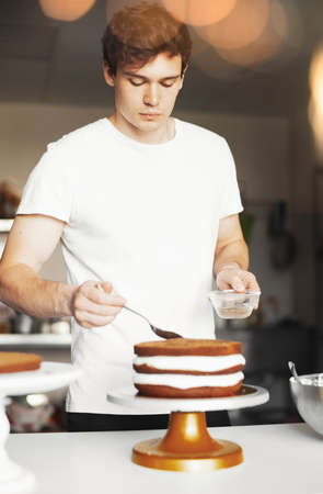 Young attractive man smearing sugar syrup on chocolate cake.の写真素材