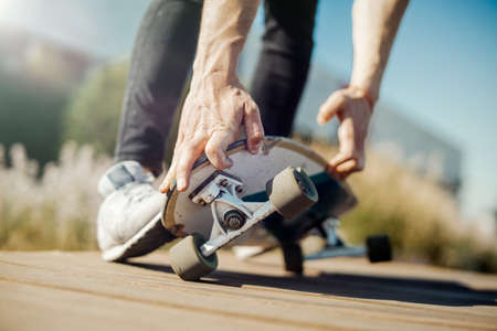 Close up of young attractive man riding longboard in the park. Man is on foreground, park is on background.の写真素材