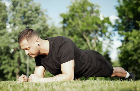 Close up of young attractive man exercising plank outdoors.