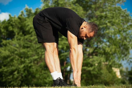Young man stretching body and legs by bending over outdoors.
