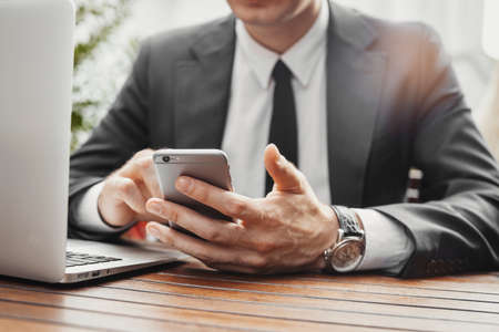 Close up of businessman looking at mobile phone and working with laptop at cafe.の写真素材