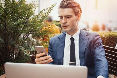 Young businessman holding mobile phone in hand and sitting next to laptop.の写真素材