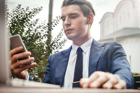 Young businessman holding mobile phone in hand and looking at screen.の写真素材