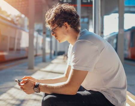 Close up of young man looking at mobile phone screen at metro station.の写真素材
