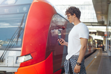 Distant plan of young man looking at mobile phone while waiting train.の写真素材