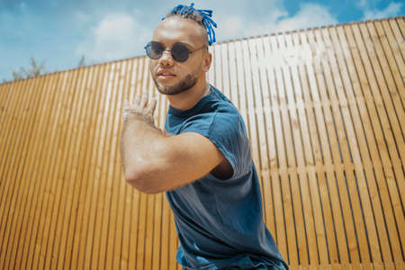 Young man with blue dreadlocks dancing reggaeton in the street. Man is on focus and foreground, wooden background is blurred.の写真素材