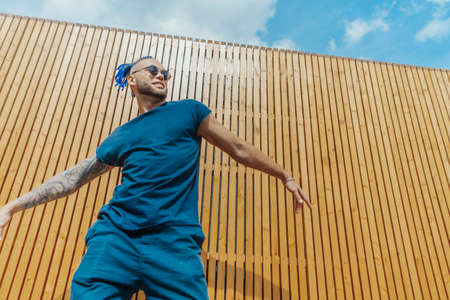 Young man with blue dreadlocks dancing reggaeton in the street. Man is on focus and foreground, wooden background is blurred.の写真素材